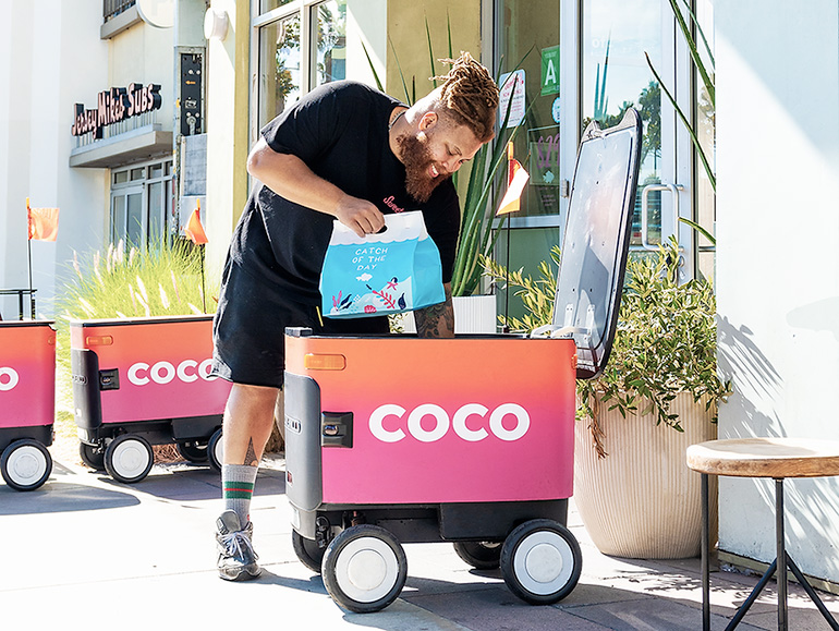 restaurant worker loads delivery item into a coco robot.