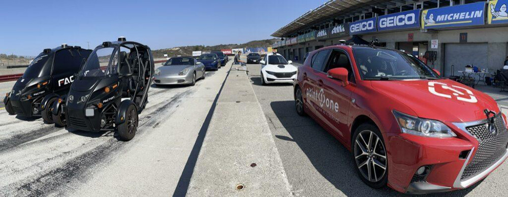 a variety of autonomous vehicles lined up on the tarmac and pits on a race track.