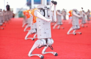 A Unitree quadruped robot balancing on its back legs with its front legs raised standing on red carpet. In the background are additional Unitree robots in the same position.