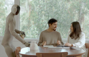 NEO Gamma placing down a teapot on a table next to two people having breakfast.