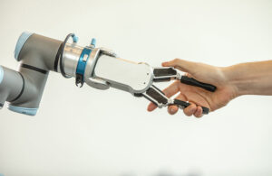 A person shaking hands with an cobot arm with an OnRobot two-fingered gripper. Odense Robotics works with Universal Robots and OnRobot.